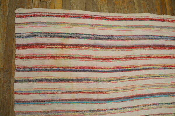 White flatweave rag rug with horizontal stripes of red, blue, gray, and yellow on wood planks.