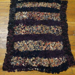 Shaggy striped rag rug in dark purple, black, and mixed colors lies on light wood planks.