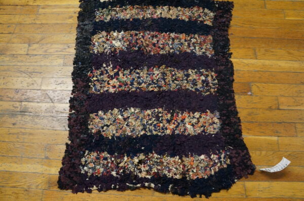 Shaggy striped rag rug in dark purple, black, and mixed colors lies on light wood planks.