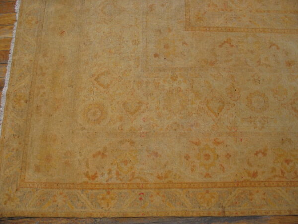 Muted gold low-pile rug with faint traditional border pattern and white fringe rests on wood floors.