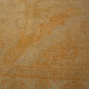 A low-contrast beige rug displays a faded classic floral pattern and bordered edge details.