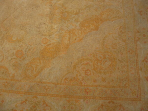 A low-contrast beige rug displays a faded classic floral pattern and bordered edge details.