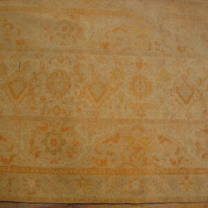 A low-pile, monochromatic tan rug featuring faded traditional patterns rests on wood flooring.