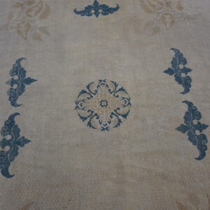 Rug surface showing blue and tan stylized scrollwork on a mottled light beige background.