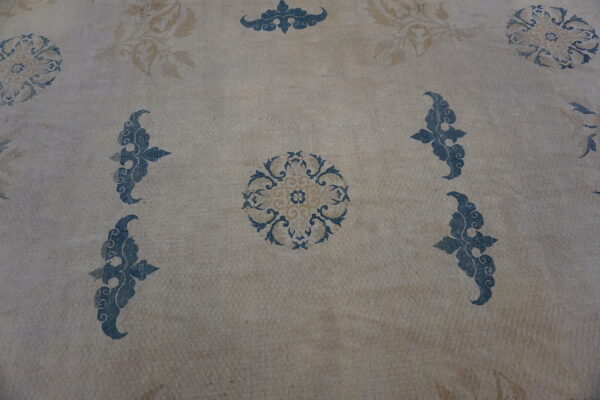 Rug surface showing blue and tan stylized scrollwork on a mottled light beige background.