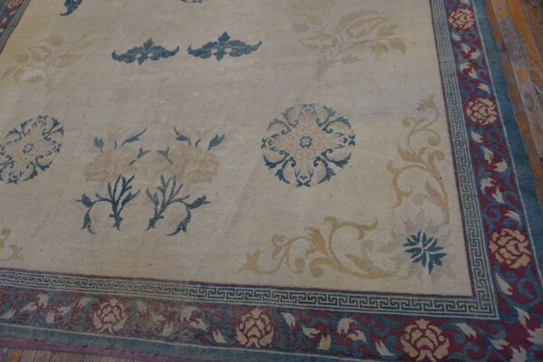 Cream rug with scattered gold and blue florals, featuring a complex burgundy border over dark wood flooring.