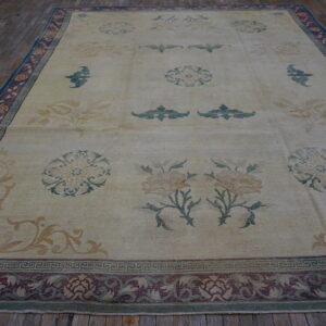 Large cream rug with muted floral motifs and a complex maroon and teal border on wood flooring.