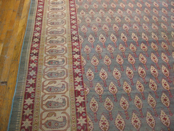 Low pile blue rug featuring ornate red and cream repeating patterns and layered borders on wood flooring.
