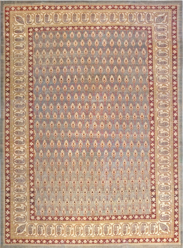 Blue-gray rug with repeating light motifs in the center field and large cream paisley borders.