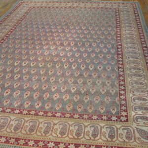 Large slate blue rug with repeating cream and red leaf motifs and complex paisley borders over wood floors.