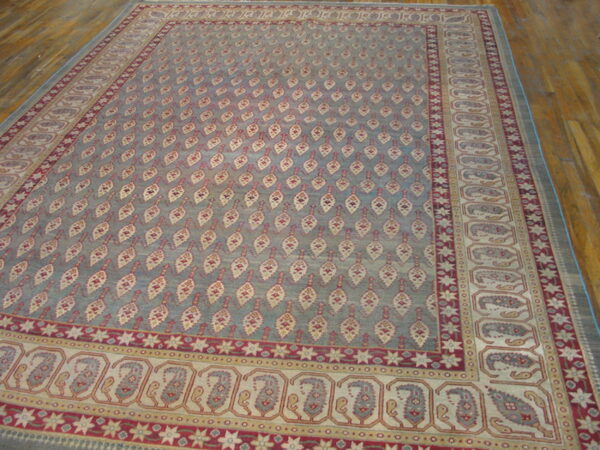 Large slate blue rug with repeating cream and red leaf motifs and complex paisley borders over wood floors.