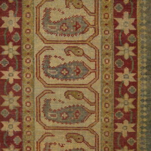 Traditional rug with red and tan geometric patterns, bordered by gray-blue stripes, resting on distressed wood flooring.