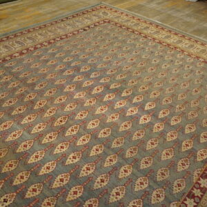 Muted blue rug with red and cream diamond patterns and an ornate border covers a distressed wood floor.