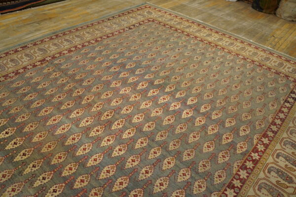 Muted blue rug with red and cream diamond patterns and an ornate border covers a distressed wood floor.