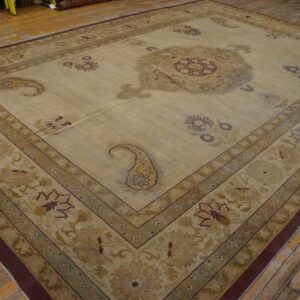 Large beige and green traditional rug with a central medallion and paisley designs on worn wood plank flooring.