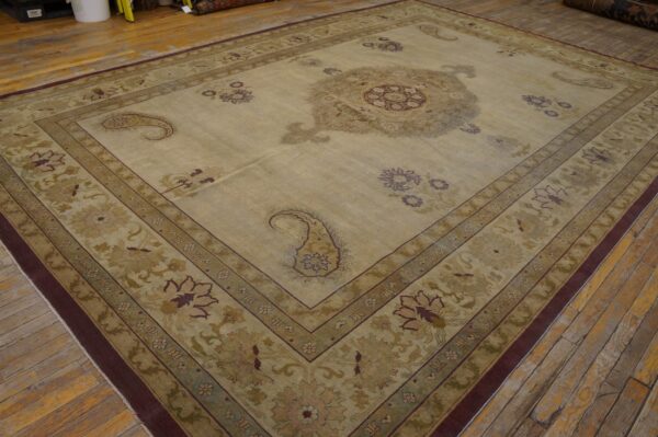 Large beige and green traditional rug with a central medallion and paisley designs on worn wood plank flooring.