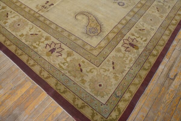 Beige and olive green rug featuring a paisley central medallion and wide floral border rests on distressed floorboards.