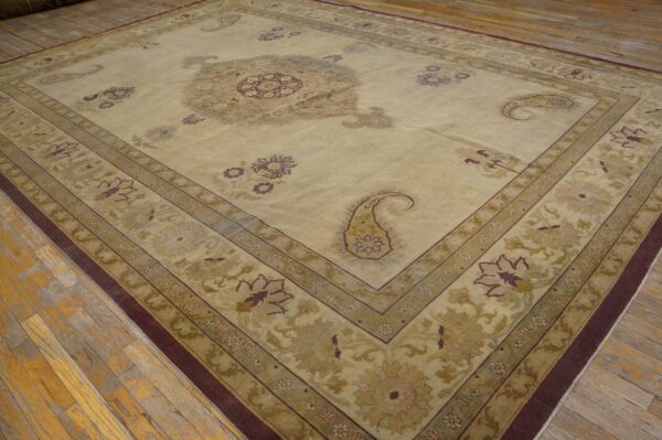 Tan rug with complex medallion and multi-layered borders in muted greens and deep purple on wood planks.