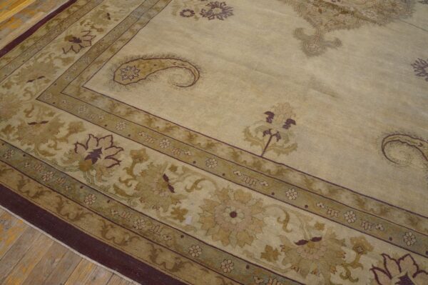Traditional patterned rug in beige, olive, and maroon lying on rustic wood plank flooring.
