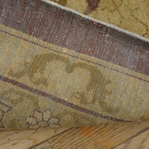 Close-up of a rug folded back, revealing a khaki and maroon striped foundation on wood flooring.