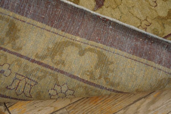 Close-up of a rug folded back, revealing a khaki and maroon striped foundation on wood flooring.