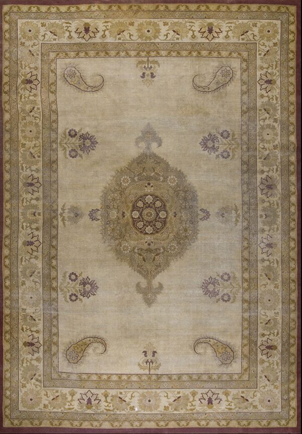 Low-pile beige rug with complex borders and a central floral medallion in gold, sage, and plum.