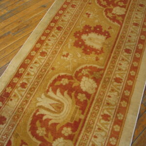 Traditional gold and rust runner featuring ornamental designs rests on distressed hardwood floors.