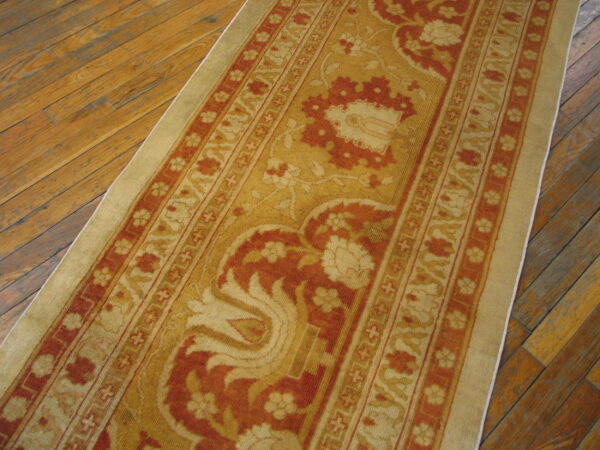 Traditional gold and rust runner featuring ornamental designs rests on distressed hardwood floors.