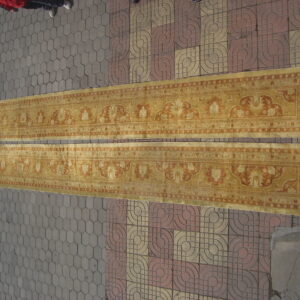 Two long, gold and terracotta runner rugs with classical patterns are placed on patterned outdoor paving.