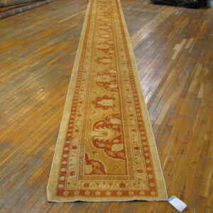 Long runner rug with elaborate gold and red traditional patterns displayed on glossy, aged hardwood flooring.
