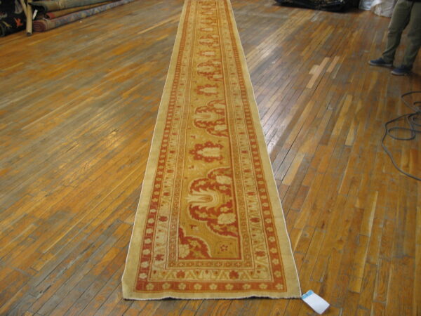 Long runner rug with elaborate gold and red traditional patterns displayed on glossy, aged hardwood flooring.