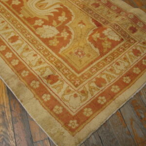 Ornate floral rug corner in golden yellow and terracotta hues lying on dark, rustic wooden planks.