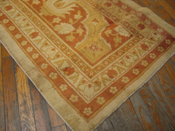 Ornate floral rug corner in golden yellow and terracotta hues lying on dark, rustic wooden planks.