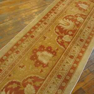 A gold and rust patterned runner rug is displayed diagonally on aged hardwood flooring.