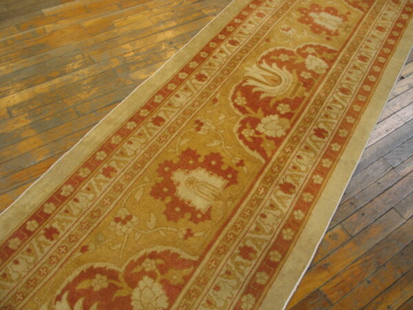 A gold and rust patterned runner rug is displayed diagonally on aged hardwood flooring.