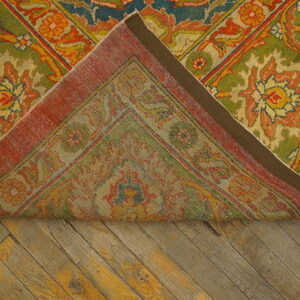 A colorful green, red, and yellow floral patterned rug is folded back on distressed diagonal wood planks.