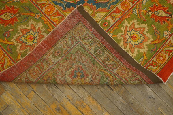 A colorful green, red, and yellow floral patterned rug is folded back on distressed diagonal wood planks.