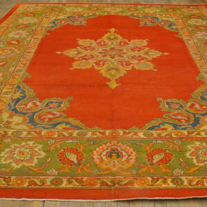 Large red medallion rug with wide olive green and multicolored borders resting on wood plank flooring.