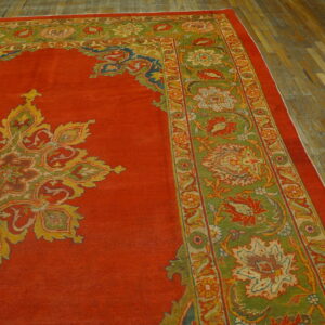 Red rug with a colorful central medallion and olive green floral borders on distressed wood flooring.