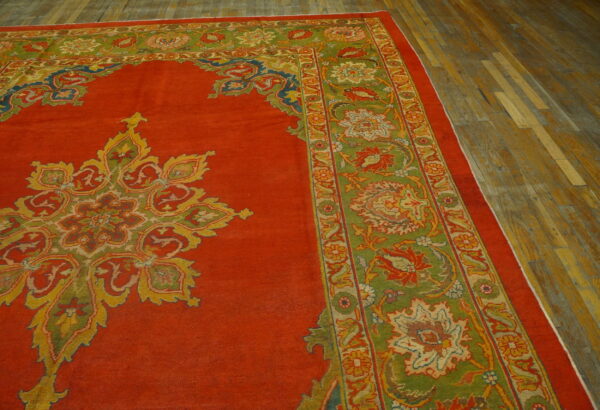 Red rug with a colorful central medallion and olive green floral borders on distressed wood flooring.