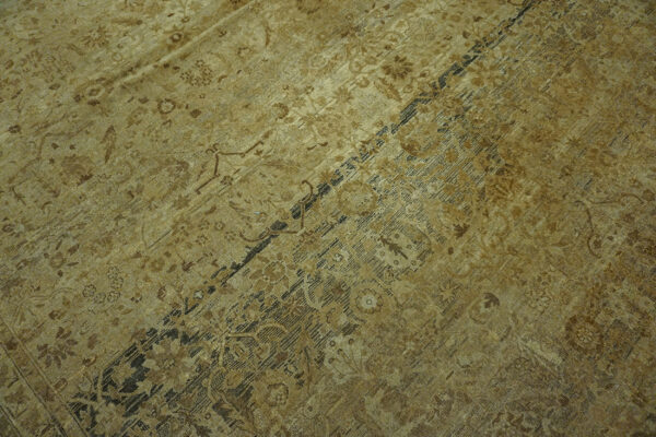 Monochromatic gold and dark brown traditional rug with a detailed border rests on distressed wood planks.