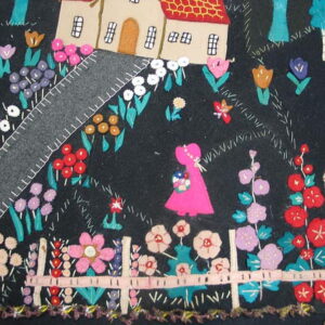 Colorful appliqué rug detail showing a stylized house, flower garden, pink figure, and cat on a dark ground.
