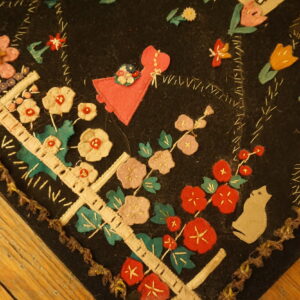 Black rug corner with colorful felt applique flowers, a pink figure, and hand-stitching on wood planks.