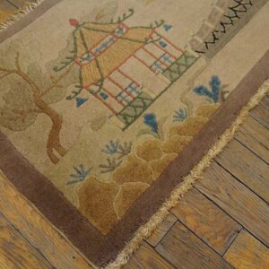 Tan rug with a raised pagoda and tree design, framed by a brown border on distressed wood floors.