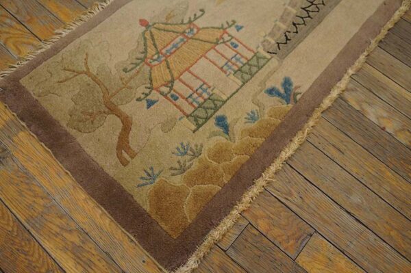 Tan rug with a raised pagoda and tree design, framed by a brown border on distressed wood floors.