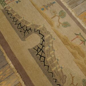 Close-up of a tan pictorial rug with a brown border and fringe on rustic wood planks.