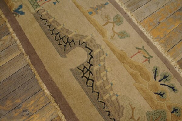 Close-up of a tan pictorial rug with a brown border and fringe on rustic wood planks.