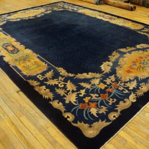 Large navy blue rug with an elaborate yellow and gold floral border rests on light wood plank flooring.