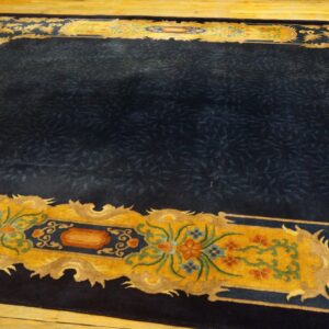 Dark blue rug with a dense vine pattern and striking yellow, ornate border resting on wood flooring.