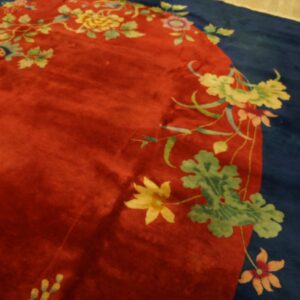Close-up of a red, lustrous rug with a navy border and vibrant yellow and green floral vine patterns.